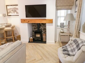 A living room with a fireplace, a television, a sofa, and a bar stool. - 8 Crown Lane (Conwy)