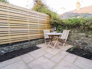 Une terrasse avec une clôture en bois, un mur en pierre et une table avec des chaises.