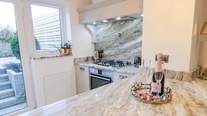 Une cuisine dotée d’un plan de travail en marbre, d’une cuisinière à gaz et d’une bouteille de vin posée sur un plateau.