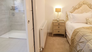 Une chambre d’hôtel dotée d’une douche en verre, d’une table de chevet avec une lampe et d’un lit avec une tête de lit à motifs.