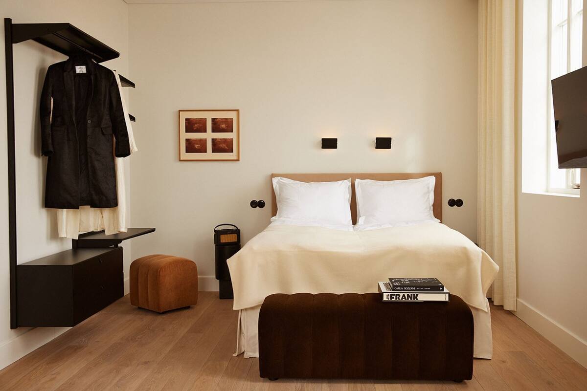 Quarto com cama, mesa de cabeceira, cabideiro, quadro emoldurado e televisão.
