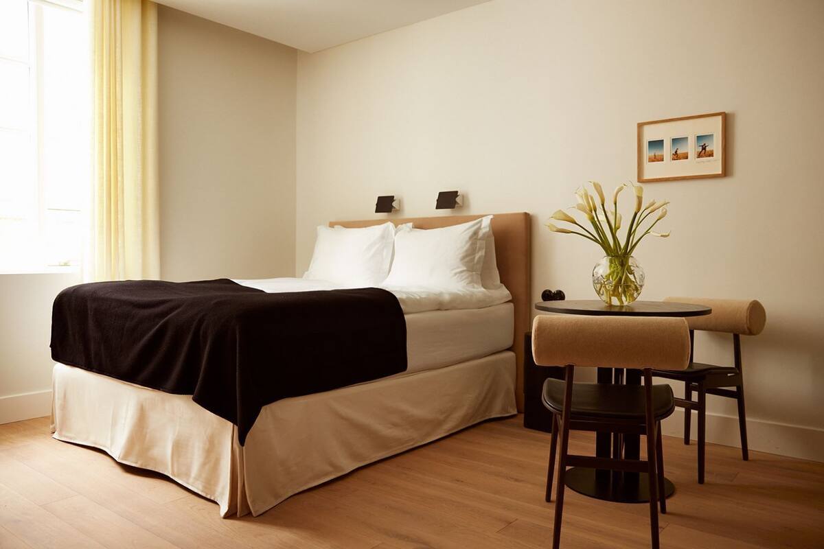 Quarto de hotel com cama, mesa de cabeceira, cadeira e uma pequena mesa com um vaso.