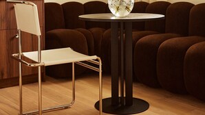 Una habitación moderna con una mesa redonda, una silla, un sofá y un jarrón con flores.