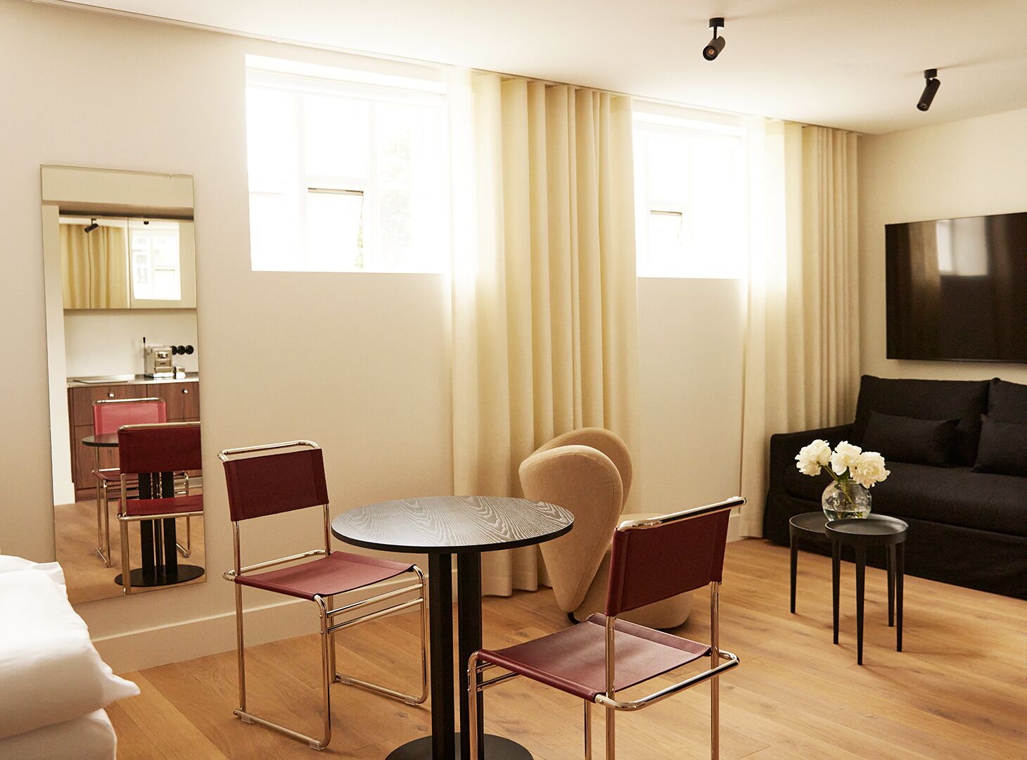 A modern living room with a round table, two chairs, a sofa, a TV, and a kitchen area in the background.