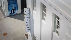 Un edificio moderno con un cartel llamativo que dice 'HOFMANN' y un gran anuncio de 'vecct' que muestra a una persona con traje.