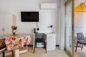 Ein Zimmer mit Schreibtisch, Stuhl, Fernseher und großem Fenster.
