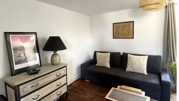 Una sala de estar con un sofá oscuro, una mesa de centro de madera, una lámpara, un cuadro enmarcado y un candelabro.
