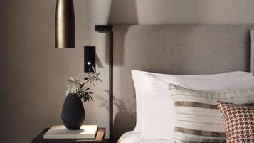Una camera da letto ordinata con comodino, lampada, vaso con una pianta, letto con cuscini e una lampada a parete.