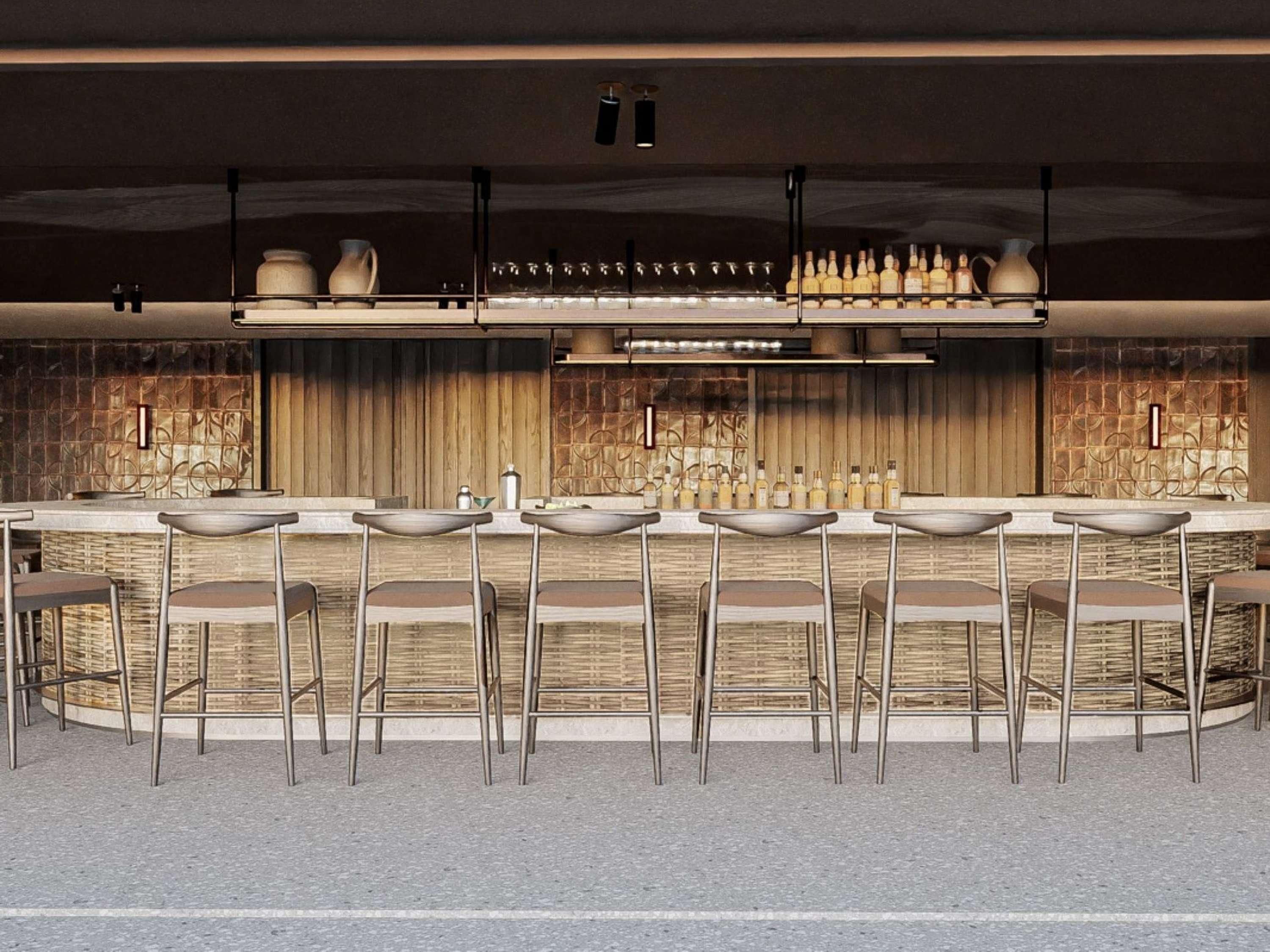A modern bar area with a long counter, multiple stools, and a variety of bottles and glasses.