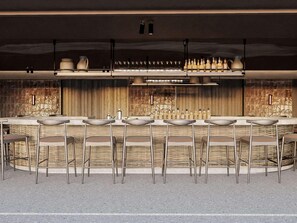 A modern bar area with a long counter, multiple stools, and a variety of bottles and glasses.