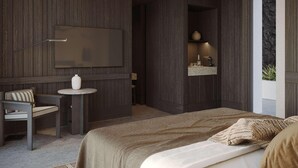 Un dormitorio moderno con una cama grande, una mesita redonda pequeña, una silla, un televisor montado en la pared y un estante empotrado con objetos decorativos.
