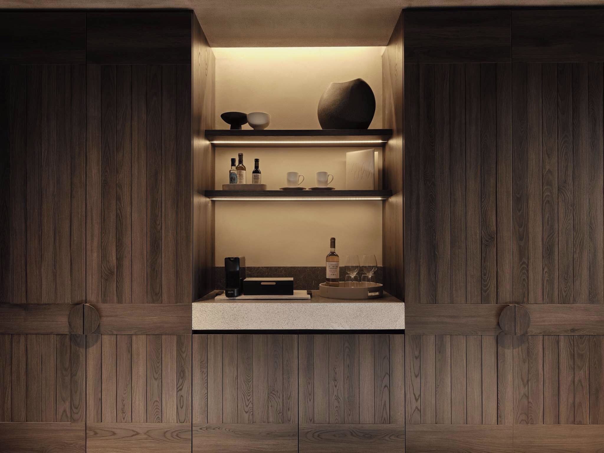 Un mueble de madera con estantes que contiene botellas, vasos y un altavoz.