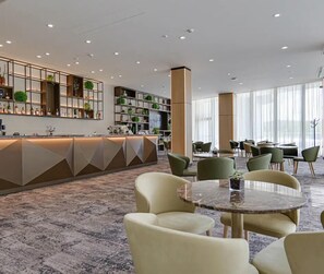A modern hotel lobby with a reception desk, seating area, and large windows.