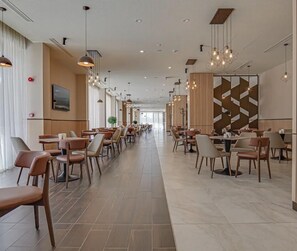 A spacious hotel lobby with multiple dining areas, modern lighting fixtures, and a large geometric wall design.