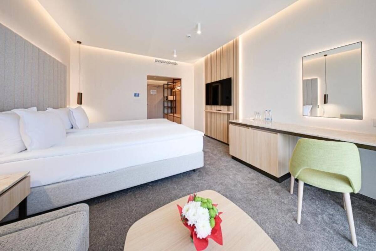A modern hotel room with a bed, a desk, a chair, a TV, and a mirror.