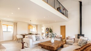 A spacious living area with a high ceiling, a dining area, and a staircase leading to an upper level. - Luxury Cotswolds Estate with Pool (Wootton)