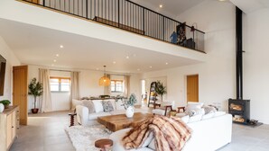 A spacious living area with a white sofa, a wooden coffee table, and a black fireplace. - Luxury Cotswolds Estate with Pool (Wootton)