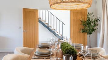 Un coin repas avec une table en bois dressée pour six personnes, un luminaire suspendu en rotin et un escalier en arrière-plan.