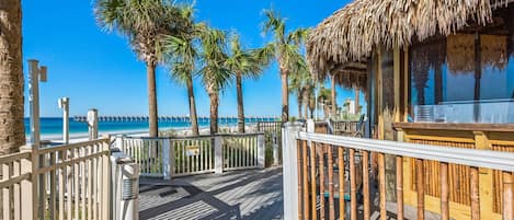 Una terraza de madera con barandilla, palmeras y vista al mar.