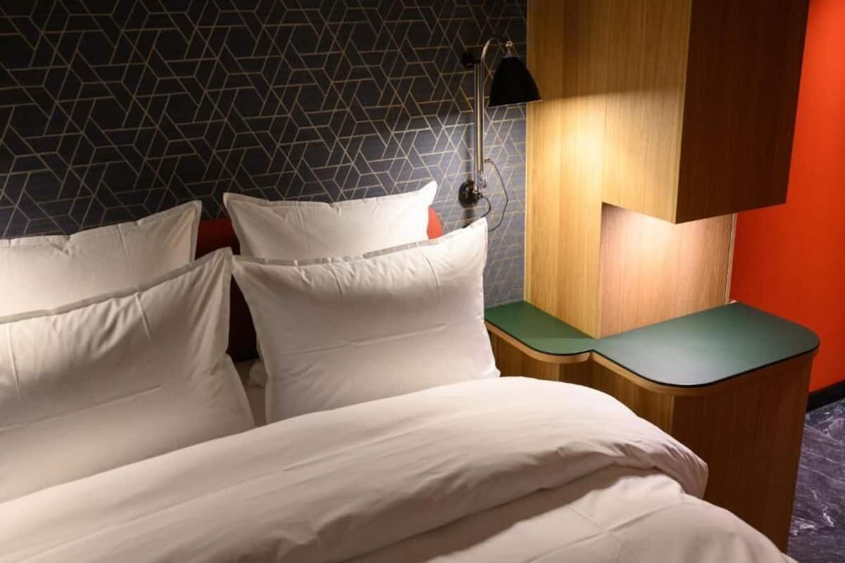 A hotel room with a bed, a nightstand, a lamp, and a geometric-patterned wall.