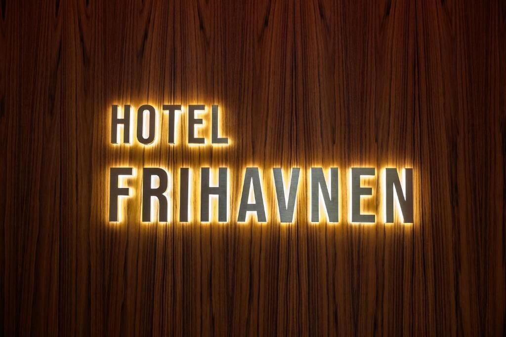 A hotel sign with the name 'HOTEL FRIHAVNEN' illuminated against a wooden background.