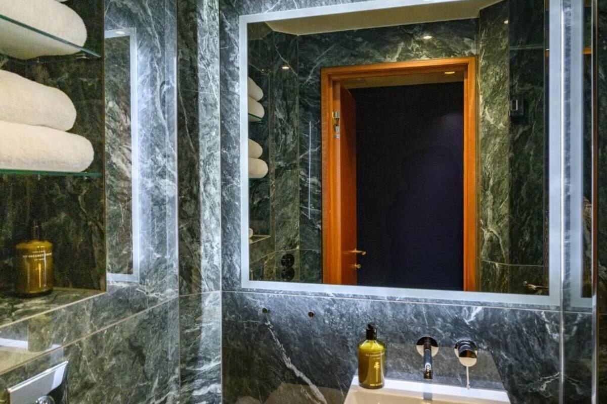 A bathroom with marble walls, a large mirror, a wooden door, and a sink with two faucets.