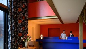 Un comptoir d’accueil avec deux employés, un vase rempli de fleurs et une chaise.