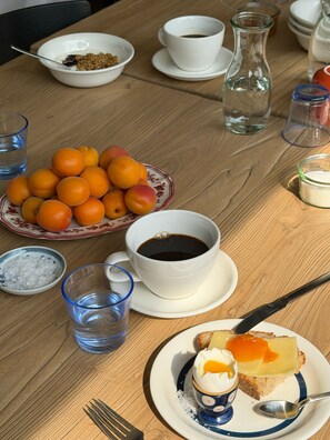 Ein Holztisch mit einer Fruchtschale, einer Kaffeetasse, einem Glas Wasser und einer kleinen Zuckerlöffel.