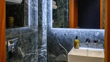 Un baño con paredes de mármol, un espejo con marco de madera, un lavamanos blanco y un perchero para toallas.