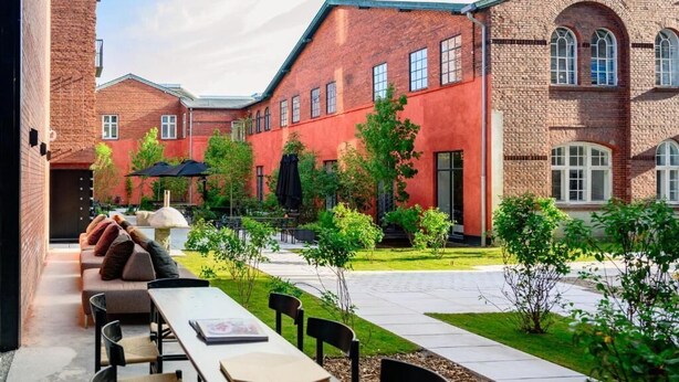 Un espace extérieur aménagé avec des tables et des chaises, entouré d’immeubles en briques et de verdure.