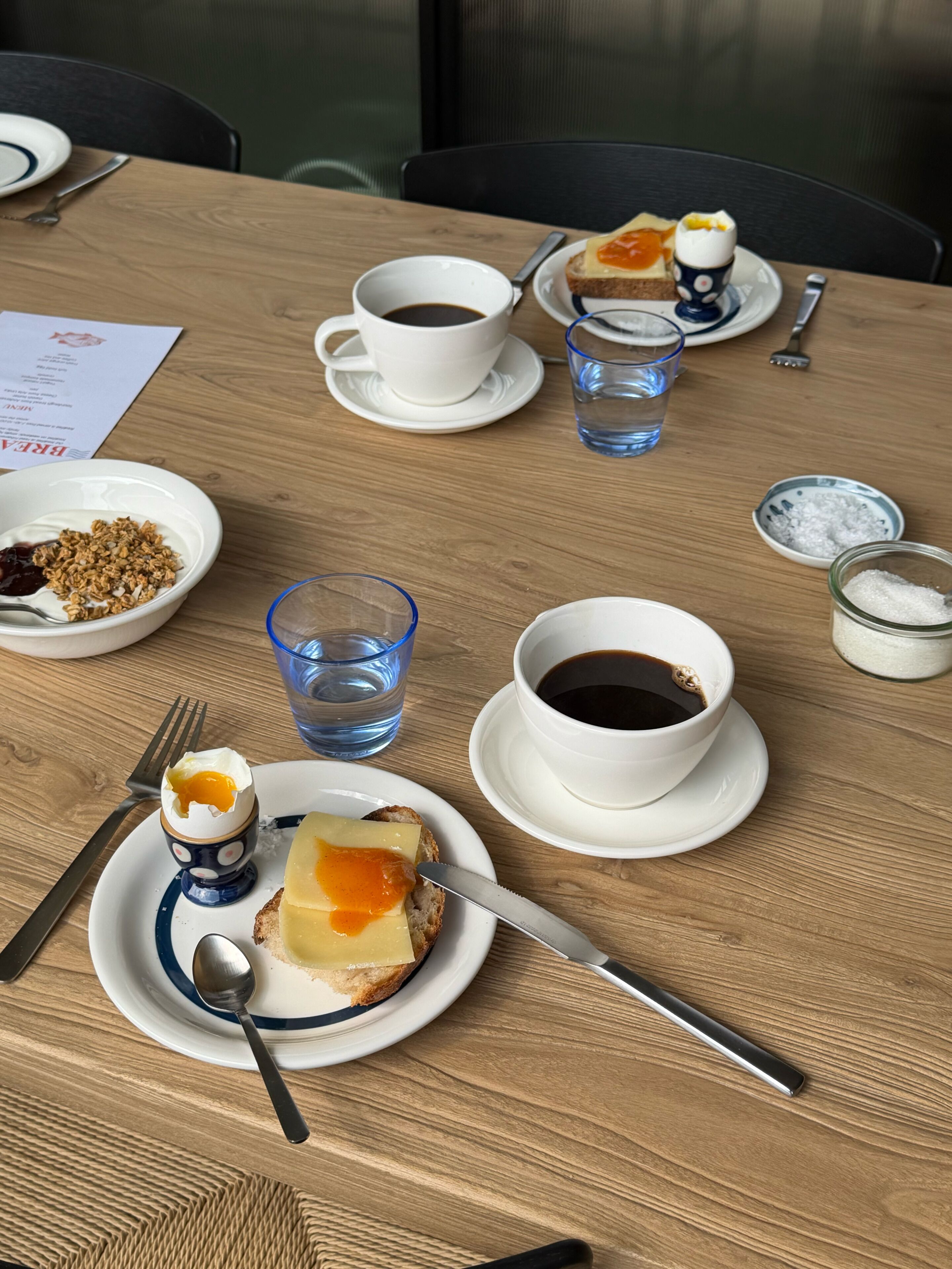A wooden table with breakfast items including toast, eggs, coffee, and water.