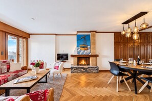 Ein geräumiges Wohnzimmer mit Kamin, Essbereich und Blick auf eine verschneite Landschaft durch ein großes Fenster.