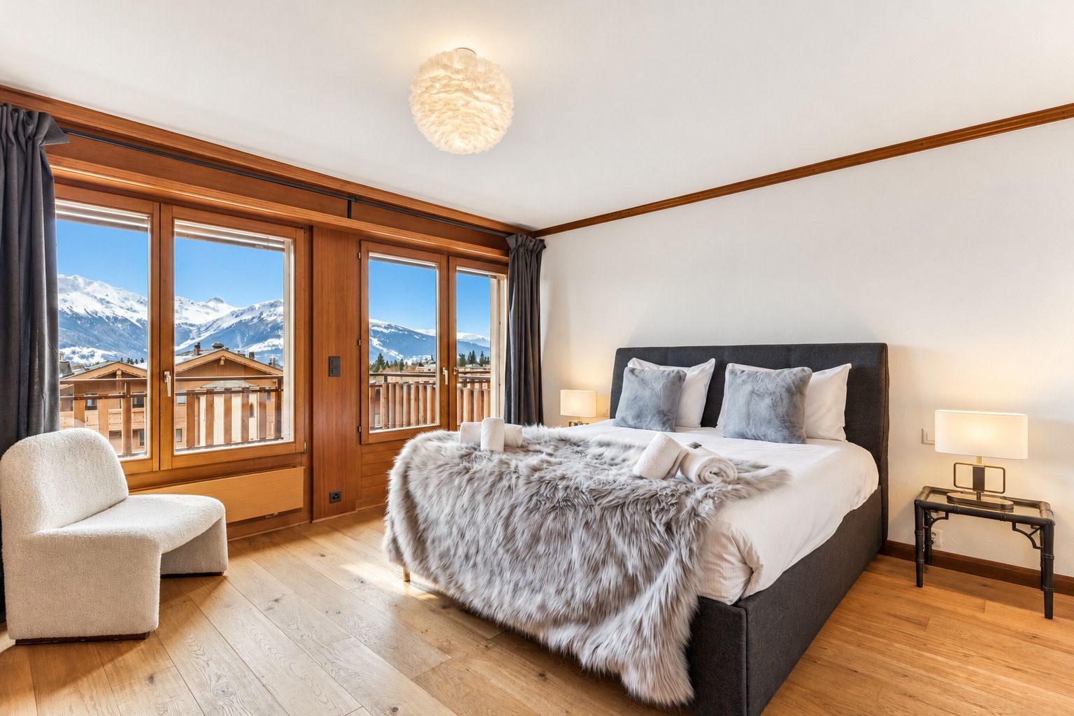 Un dormitorio con una cama grande, una silla, una mesita de noche y vistas a las montañas desde la ventana.