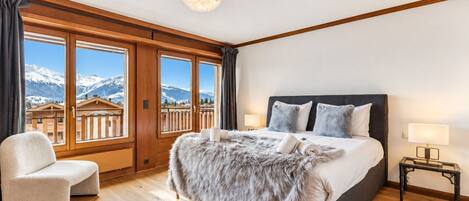 A bedroom with a large bed, a chair, a nightstand, and a view of mountains through the window.