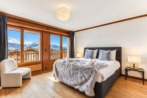 Ein Schlafzimmer mit einem großen Bett, einem Sessel, einem Nachttisch und Blick auf Berge durch das Fenster.
