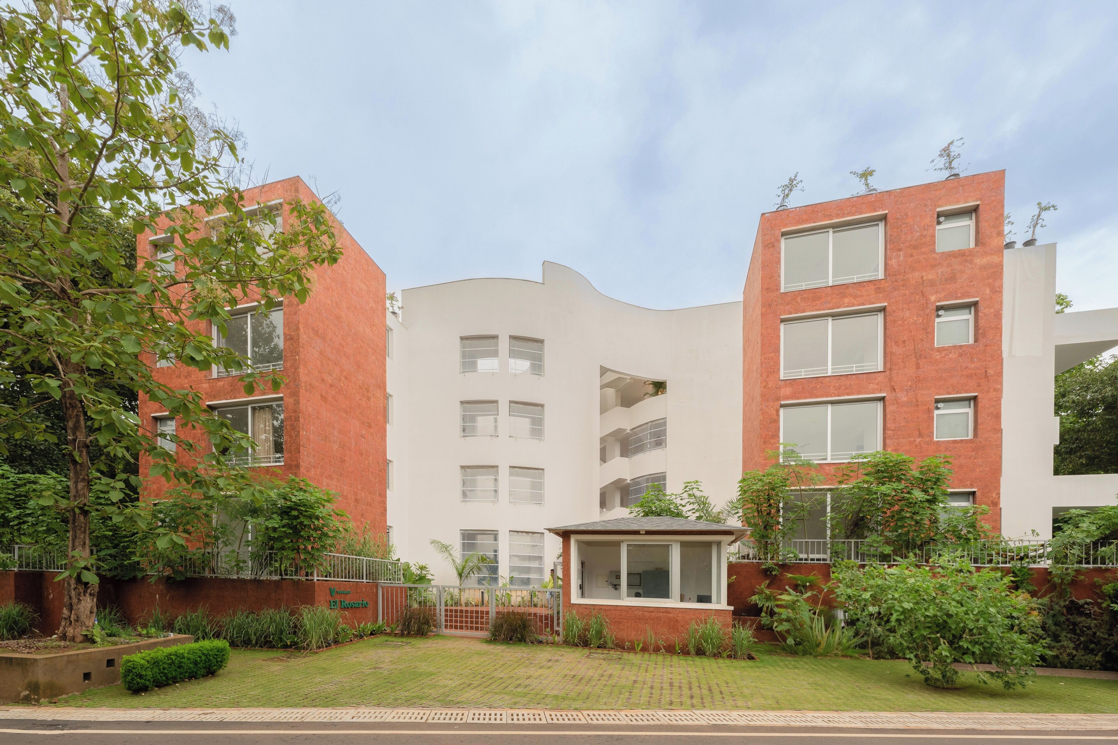 A modern building with a mix of brick and white facades, multiple windows, and a small garden area with greenery.