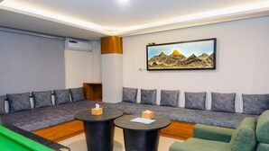 Une pièce avec une table de billard, un canapé vert, un fauteuil vert et un tableau accroché au mur.