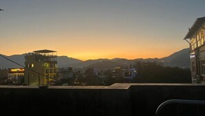 Une vue sur une ville au coucher du soleil, avec des bâtiments et des montagnes en arrière-plan.
