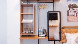 Une chambre d’hôtel avec une étagère en bois, un téléviseur à écran plat, un lit doté d’une tête de lit à motifs et un tableau représentant un bâtiment accroché au mur.