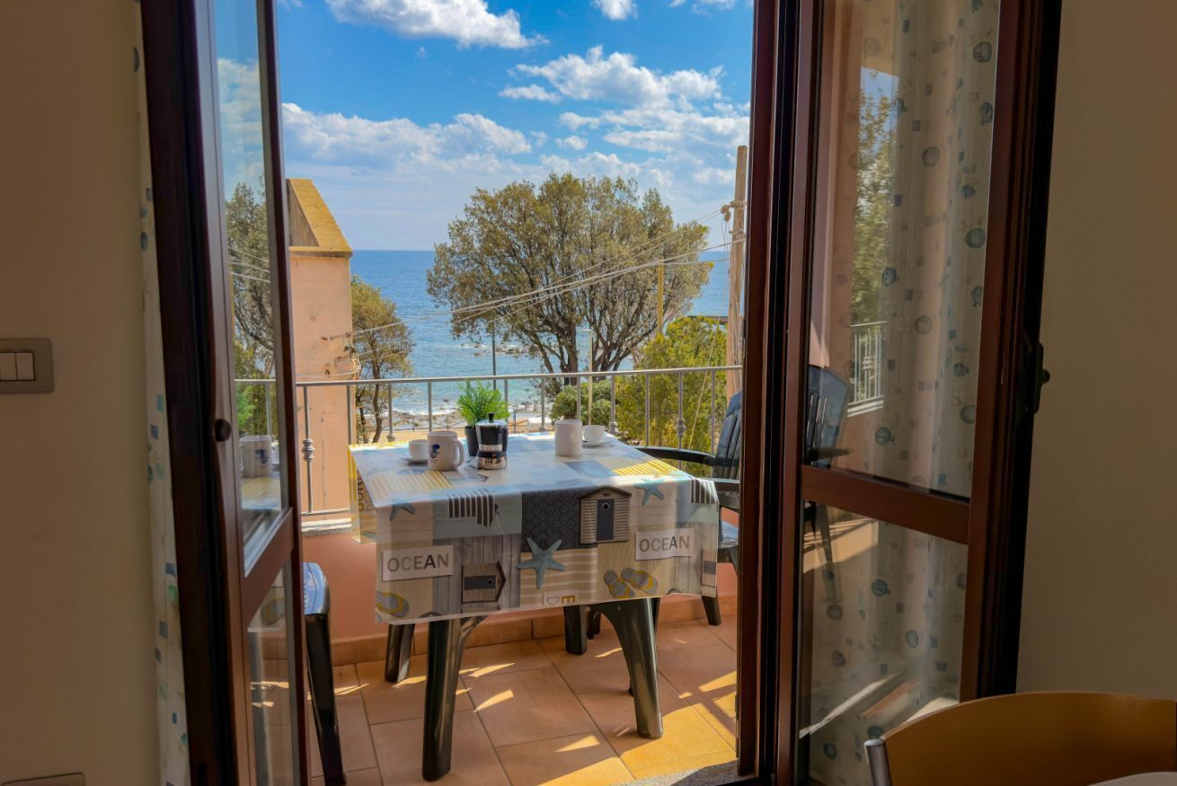 A balcony with a table set for two, overlooking a coastal view.