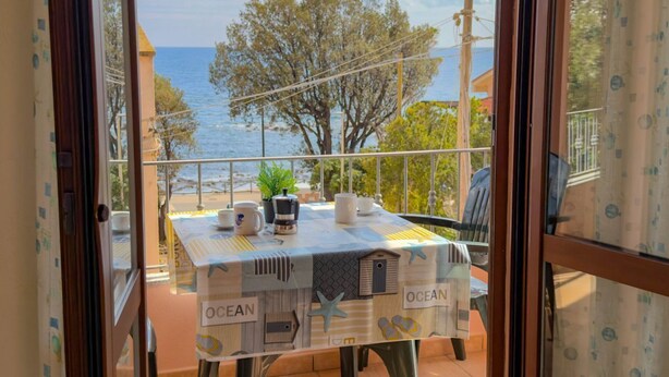 Ein Balkon mit Tisch für zwei Personen, mit Blick auf das Meer, Bäume und den Ozean.