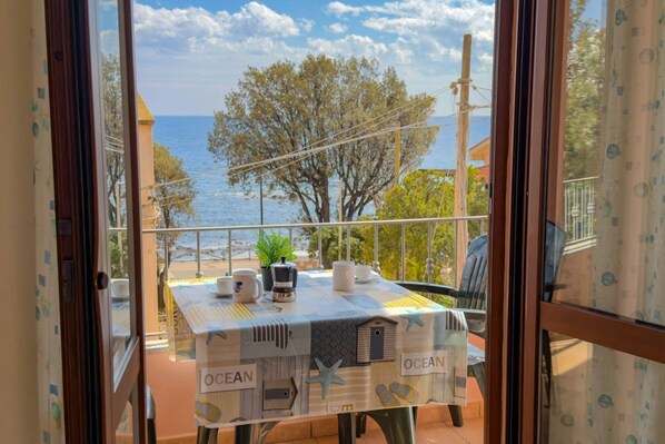 A balcony with a table set for two, overlooking the sea, with a view of the ocean and trees. - Appartamento Lido Residence 1 (Cala Gonone)