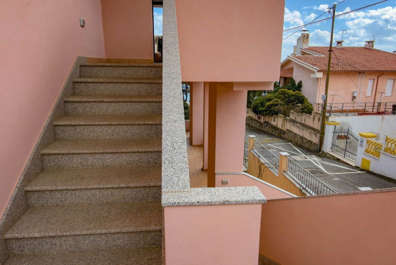 A staircase leading to a pink building with a view of a street and neighboring houses.
