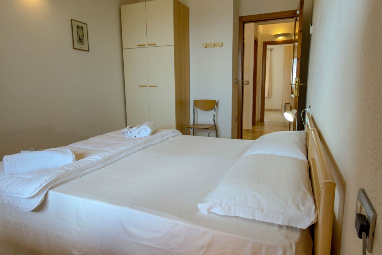 Un letto rifatto con cuscini e coperta, un armadio in legno, una sedia e uno specchio.