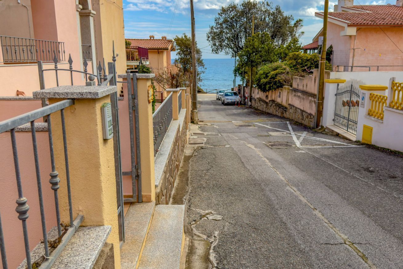 A narrow street with a sea view, a gate, and a parked car.