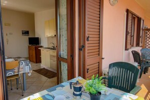 A room with a dining table, chairs, a potted plant, a coffee maker, and a television. - Appartamento Lido Residence 1 (Cala Gonone)