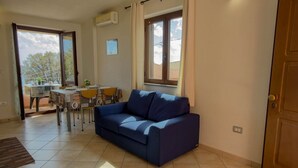 Ein Wohnzimmer mit einer Couch, einem Esstisch mit Stühlen, einem Fenster mit Vorhängen und einer Klimaanlage.