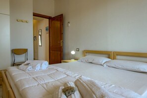 A hotel room with a large bed, a wooden headboard, a bedside table with a lamp, and a chair. - Appartamento Lido Residence 1 (Cala Gonone)