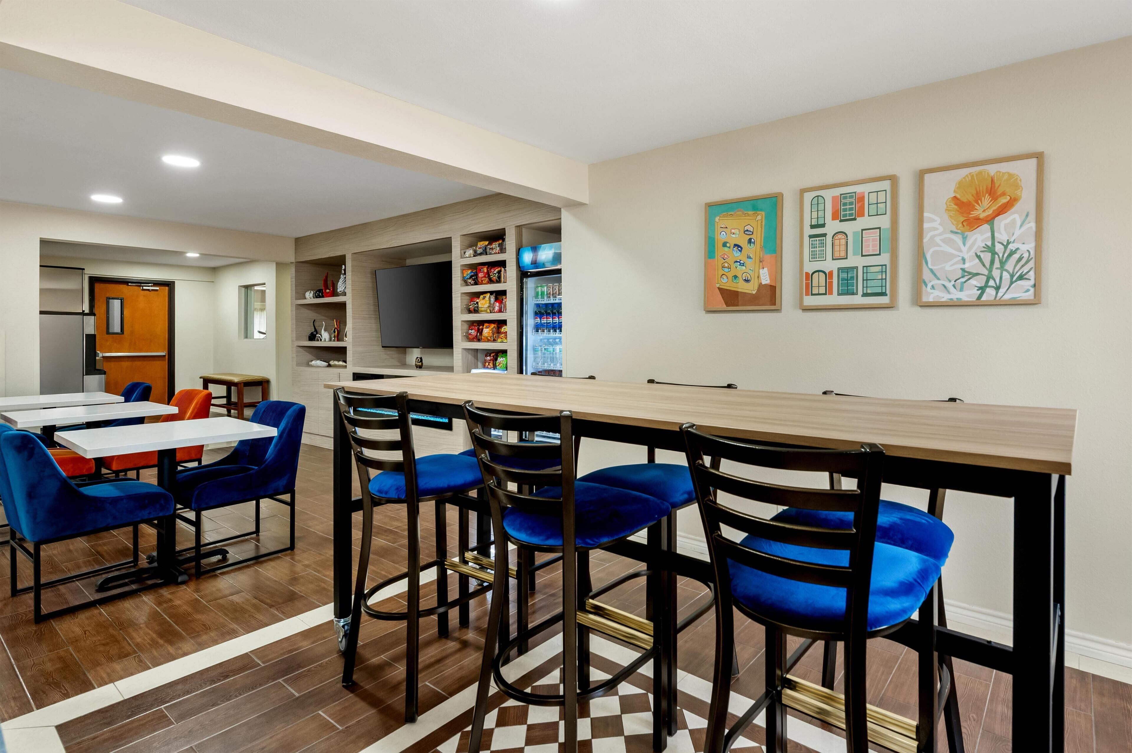 Una cocina moderna con una barra alargada, taburetes azules y un refrigerador lleno de bebidas.