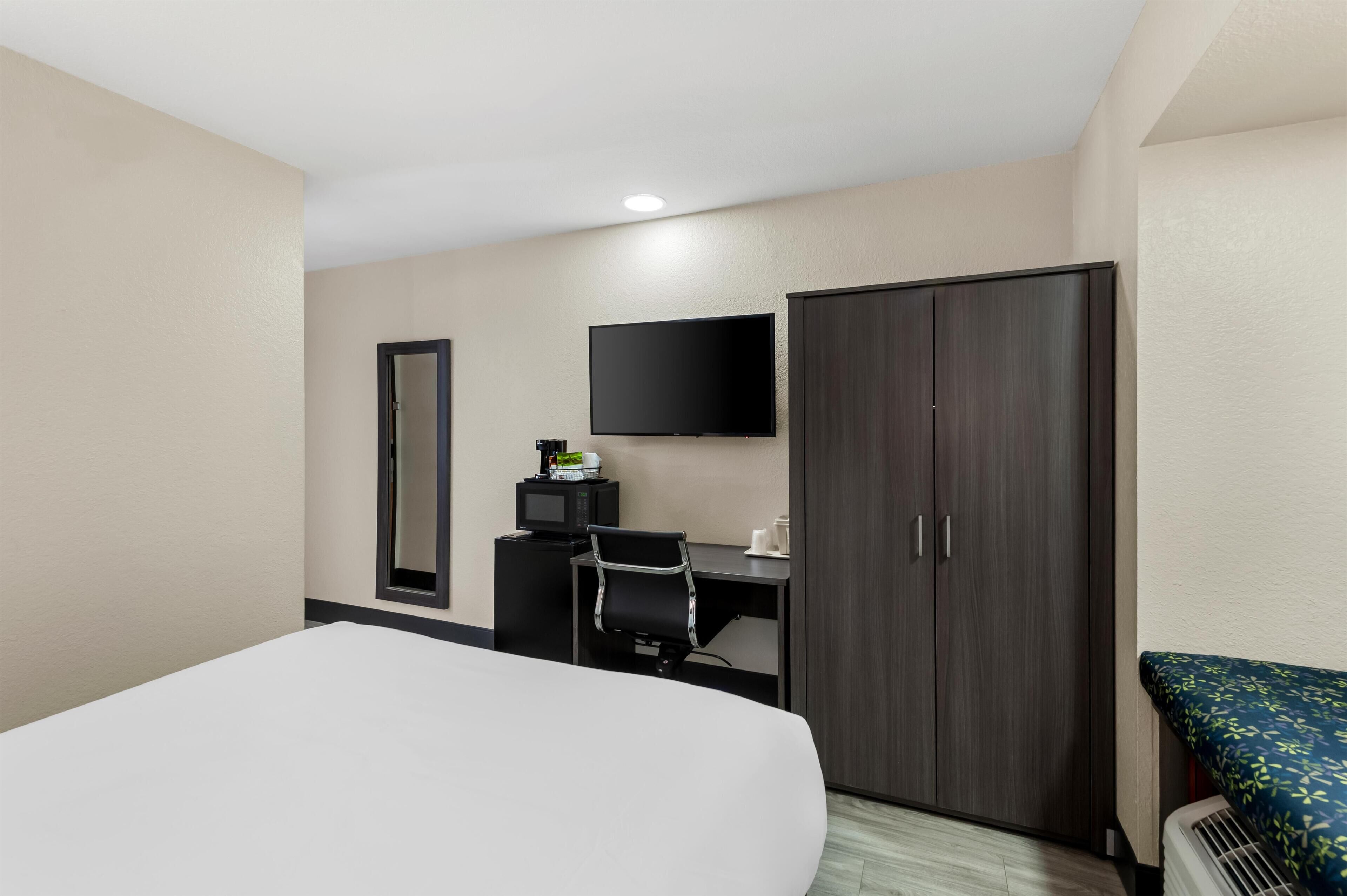 Una habitación de hotel con una cama, un escritorio con computadora, televisor y armario.